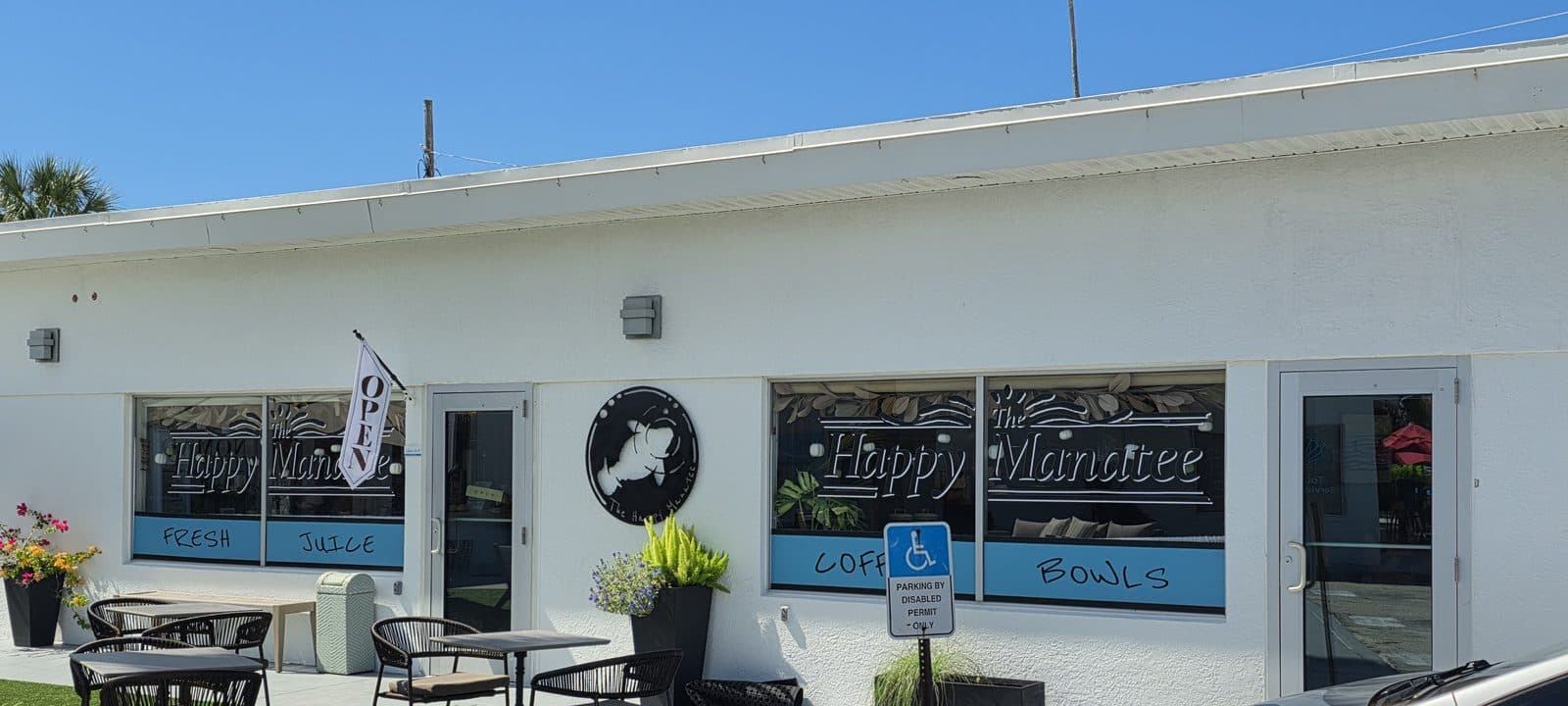 The white front of The Happy Manatee cafe with outdoor tables and a blue Open sign