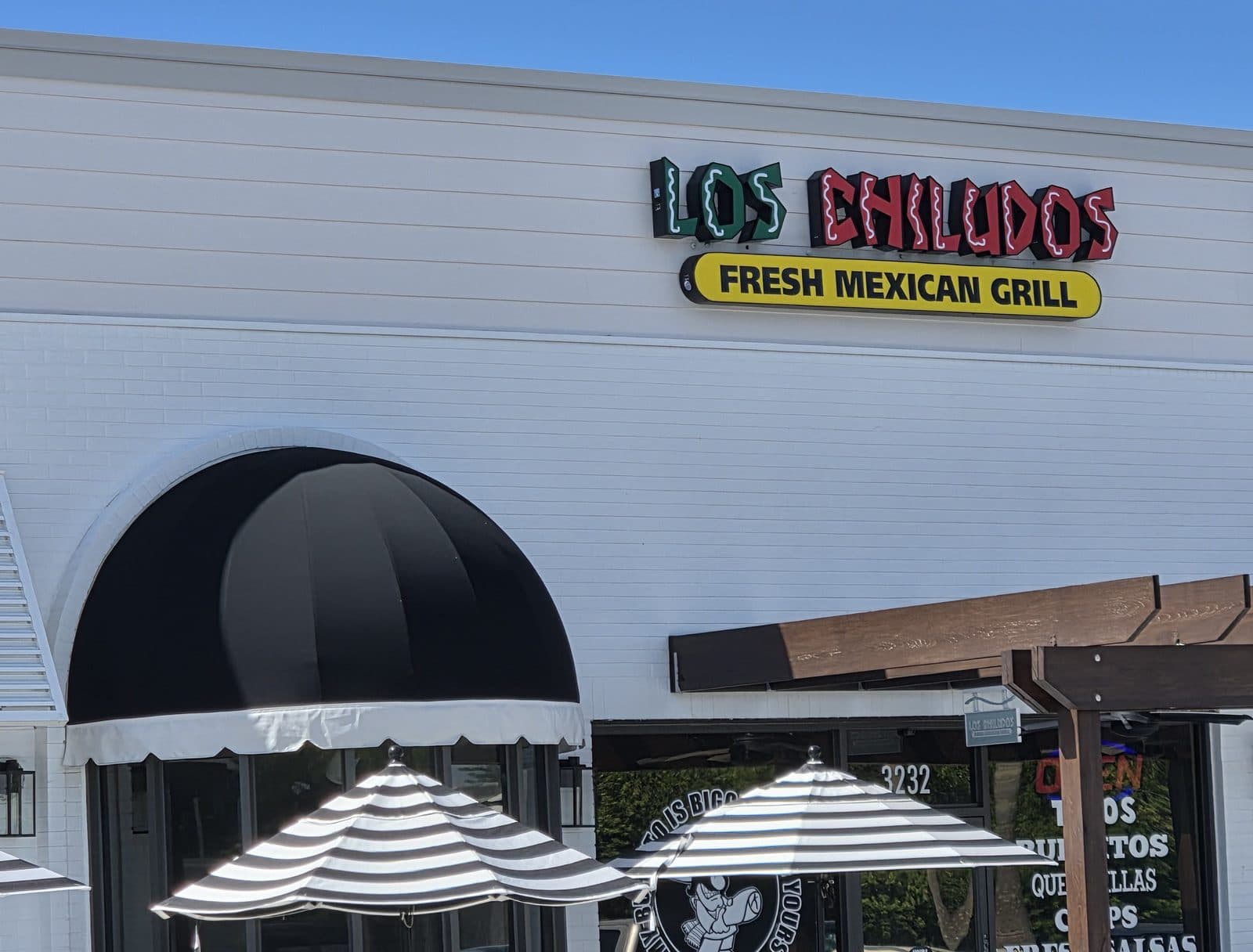 The Los Chiludos Fresh Mexican Grill sign above a black awning and striped umbrellas