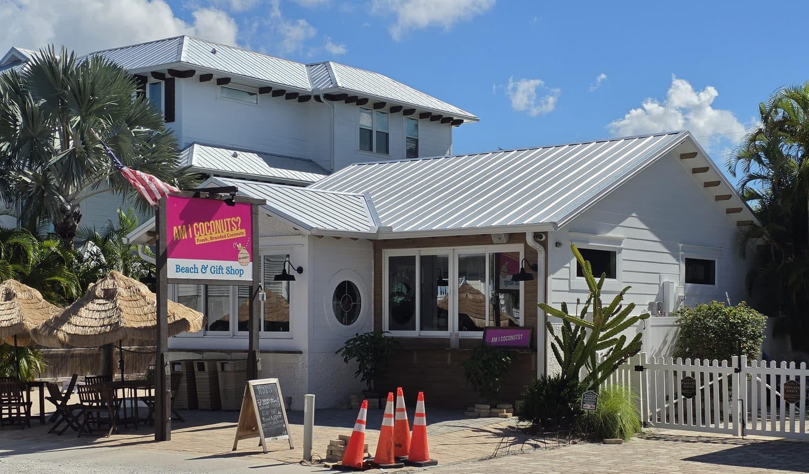 The Am I Coconuts? beach and gift shop on Pine Ave, a white cottage with a pink sign, thatch umbrellas and a white picket fence