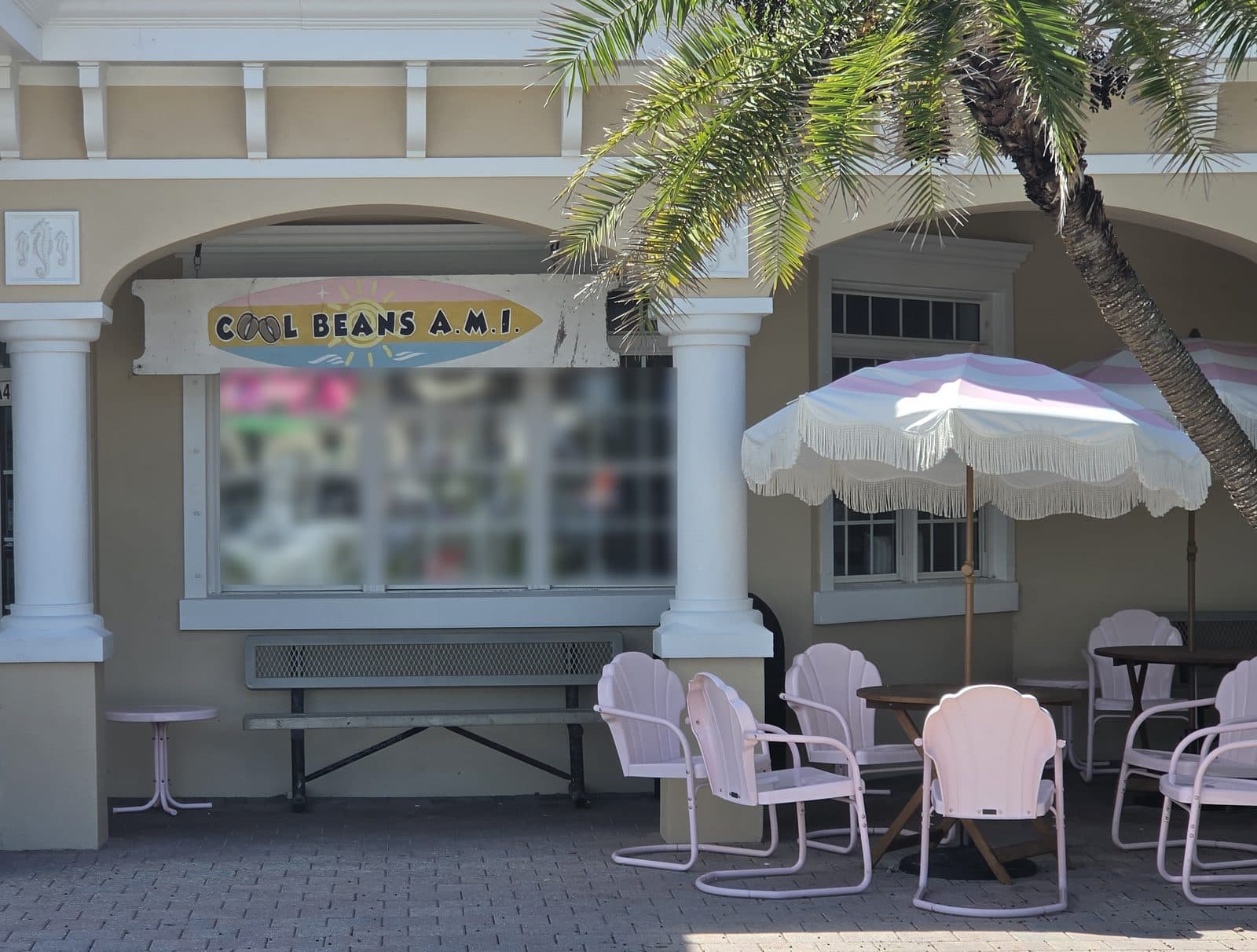 Cool Beans A.M.I. under its surfboard sign, with pink beach chairs and a fringed umbrella on the brick patio