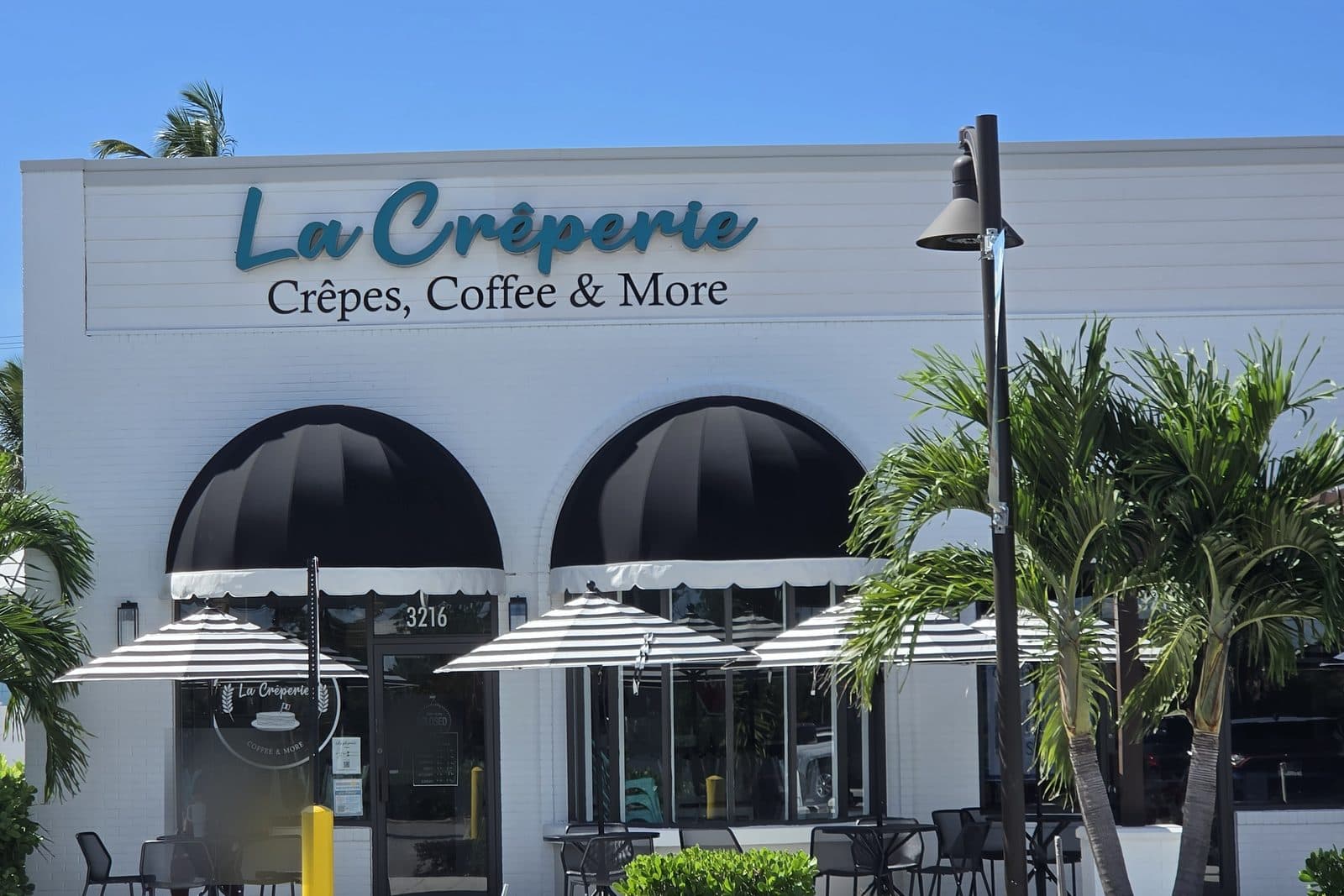 La Crêperie, a white storefront with black awnings and striped umbrellas out front