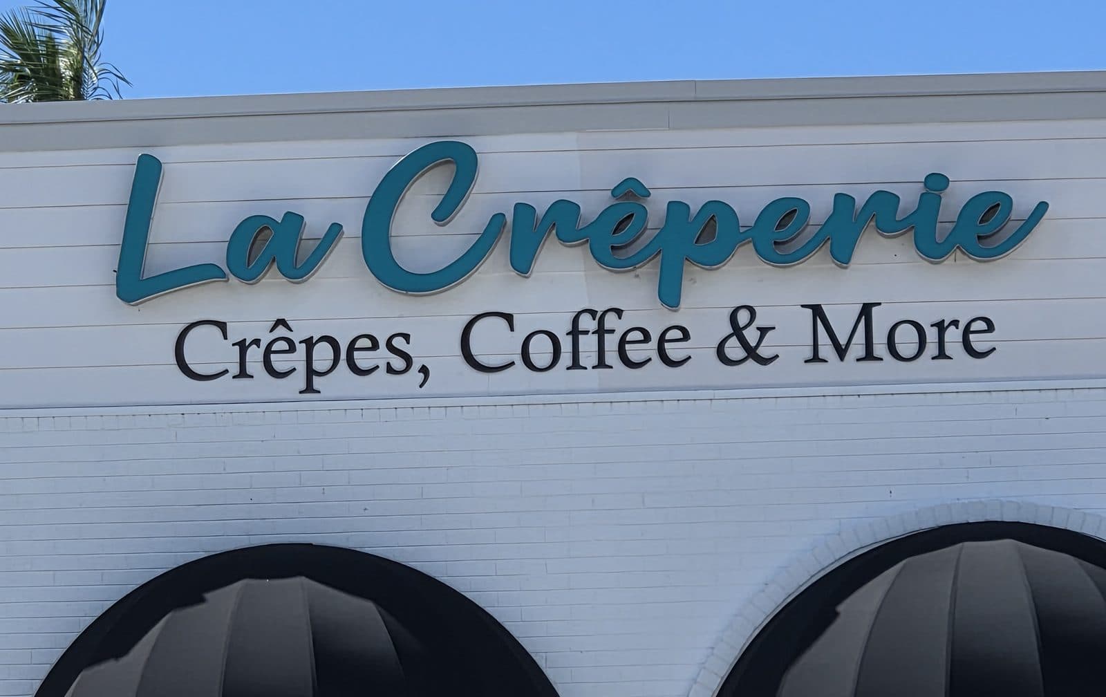 The teal La Crêperie, Crêpes, Coffee and More sign above two black awnings