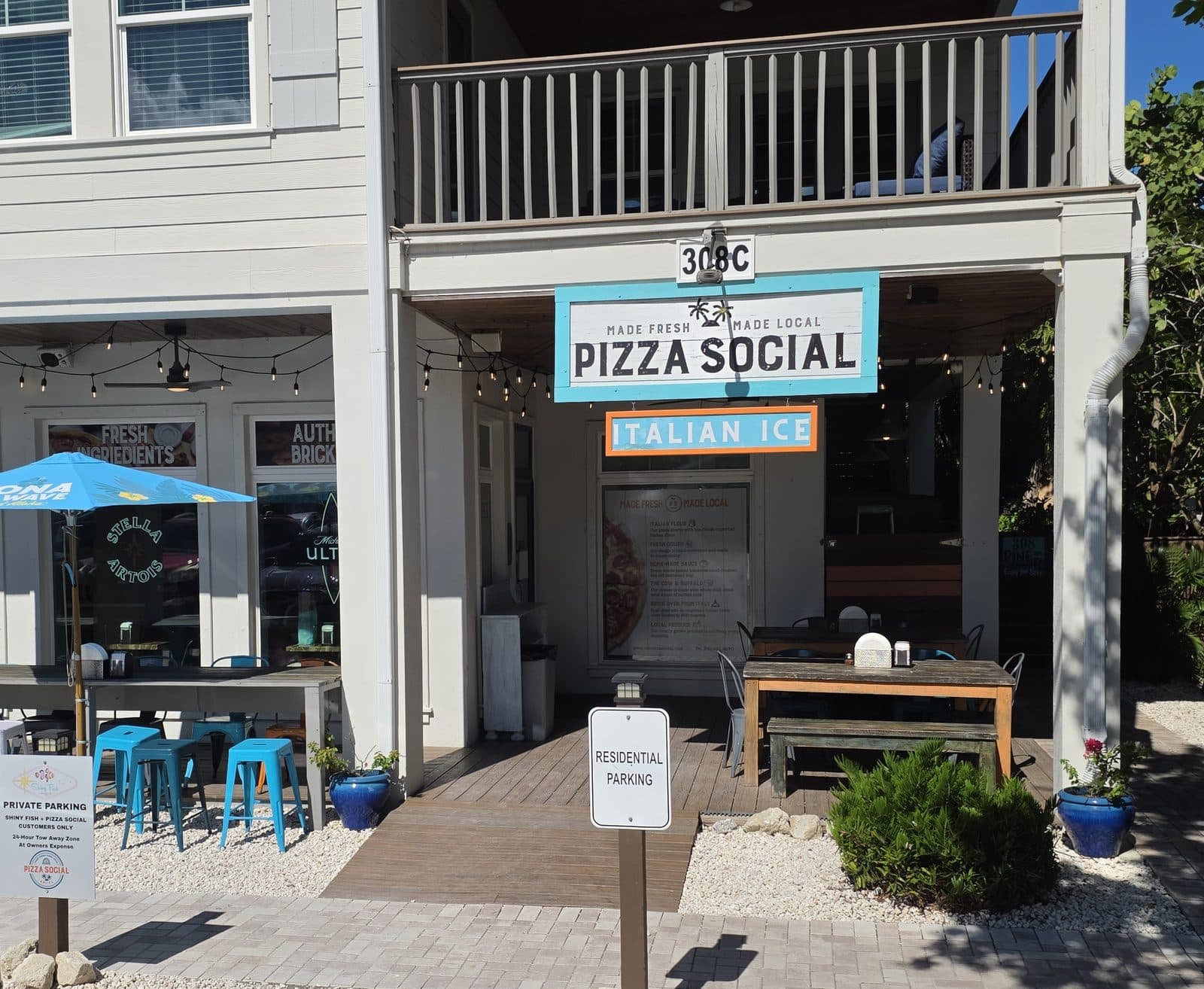 The teal Pizza Social sign and Italian Ice sign on Pine Ave, with blue stools under the porch
