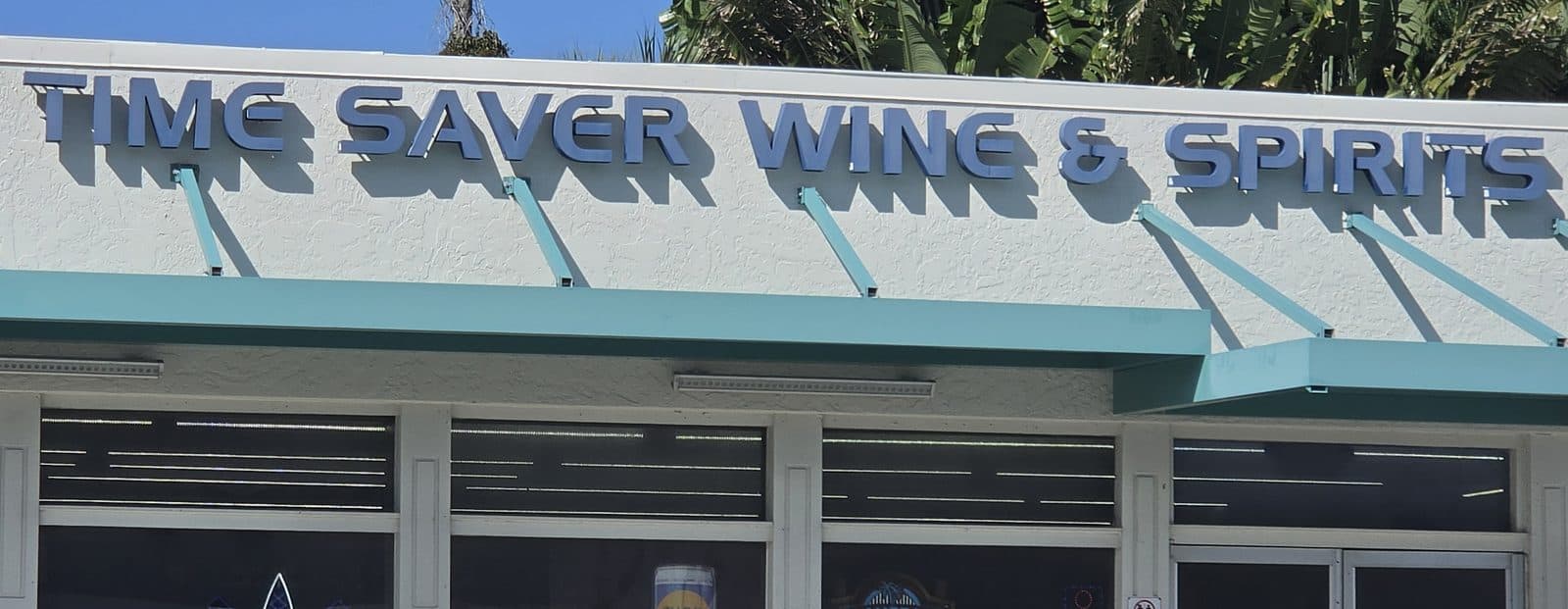 The Time Saver Wine and Spirits sign above a teal awning and a row of windows with beer signs