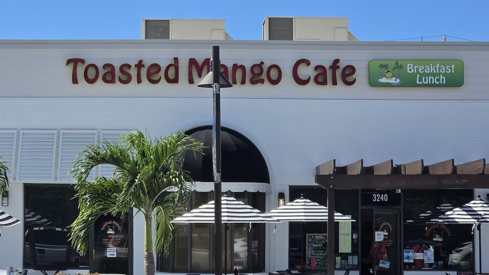 The Toasted Mango Cafe sign and striped umbrellas on East Bay Dr